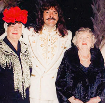 Shawn Rae in an ornate white suit posing with two elegantly dressed guests