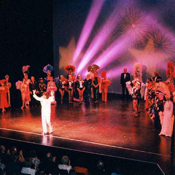 Shawn Rae performing on a grand stage under spotlights with a full ensemble cast